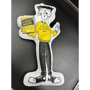 May include: A white, cartoon-style figure holding a book titled "Dummies Books." The figure wears a yellow sweater with the text "Every Day The Dummies Way" and black pants. The figure is a promotional item.