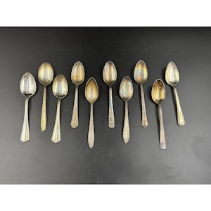 May include: An assortment of antique silver spoons, each with a unique design. The spoons vary in size and shape, with some featuring ornate detailing on the handles. The spoons are arranged on a black surface, showcasing their reflective qualities.