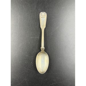 May include: A silver spoon with an oval bowl and a long, slender handle. The handle features a decorative design at the top. The spoon is likely vintage or antique, and is made of a shiny, reflective metal.