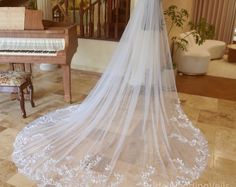 May include: A long, white bridal veil with delicate floral embroidery. The veil is made of soft tulle and has a scalloped edge.