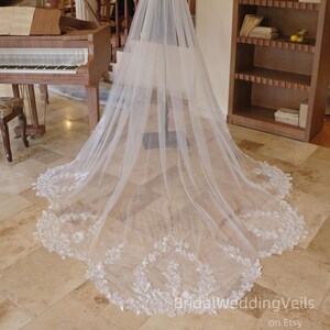 Peut inclure: Un long voile de mariée blanc avec une délicate bordure en dentelle florale. Le voile est fait d'un tissu transparent et est exposé à l'intérieur. Le texte "BridalWeddingVeils on Etsy" est visible en bas de l'image.