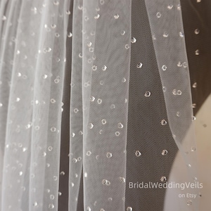 May include: Close-up of a white tulle veil with scattered, sparkling embellishments. The veil is sheer and delicate, with a soft, flowing texture. The text "BridalWeddingVeils on Etsy" is visible in the bottom right corner.