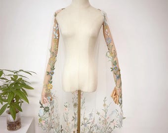 May include: A white tulle veil with floral embroidery in shades of blue, pink, yellow, and green. The veil is displayed on a white mannequin.