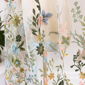 Pode incluir: Tecido de tule branco com desenhos florais bordados em tons de verde, azul, amarelo e rosa. As flores est&atilde;o espalhadas por todo o tecido e t&ecirc;m um visual delicado e rom&acirc;ntico.