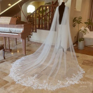 Puede incluir: Un velo de novia largo y blanco con un delicado borde de encaje. El velo está drapeado sobre una silla y fluye hasta el suelo.