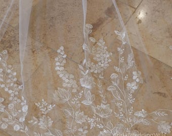 May include: A white bridal veil with delicate floral embroidery. The veil is made of soft tulle and features a delicate floral pattern with small white flowers and leaves. The veil is perfect for a romantic wedding.
