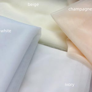 May include: Four swatches of tulle fabric in different colors: white, ivory, beige, and champagne.