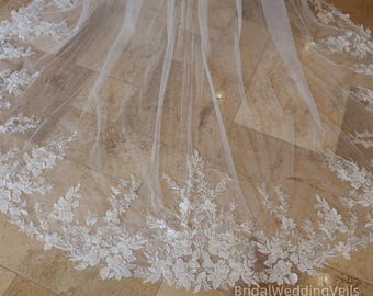 May include: A white bridal veil with intricate floral lace detailing along the edge. The veil is made of a sheer, flowing fabric, and the lace features delicate flower and leaf patterns. The text "BridalWeddingVeils on Etsy" is visible.
