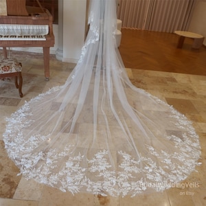 May include: A long, white bridal veil with a delicate floral lace trim. The veil is made of soft tulle and has a cathedral length.