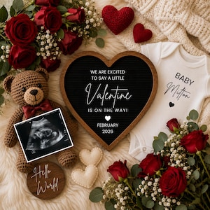 May include: A heart-shaped black letter board with white text reading WE ARE EXCITED TO SAY A LITTLE Valentine IS ON THE WAY! FEBRUARY 2026, a white baby bodysuit, a brown crochet teddy bear, an ultrasound scan, and red roses.