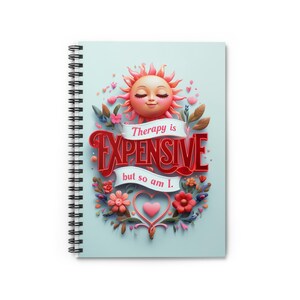 May include: A spiral bound notebook with a light blue cover featuring a cartoon sun with closed eyes and a pink heart. The sun is surrounded by pink and green flowers and leaves. The text "Therapy is Expensive but so am I." is written in red and pink letters.
