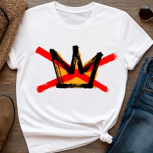 Peut inclure: T-shirt blanc avec un motif de couronne noire, rempli d'orange et de jaune, et traversé par deux coups de pinceau rouges. Un t-shirt graphique décontracté.