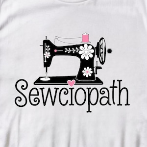 Peut inclure: T-shirt blanc avec un motif de machine à coudre noire, des détails floraux et une bobine de fil rose. Le texte "Sewciopath" est écrit en police script en dessous.