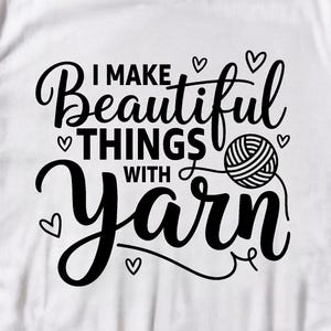 May include: White t-shirt with the text "I Make Beautiful Things With Yarn" in black script. The design includes hearts and a yarn ball. The shirt is paired with blue jeans and white sneakers.