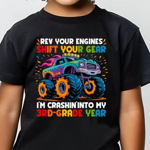 May include: Black t-shirt with a colorful monster truck graphic and the text "REV YOUR ENGINES SHIFT YOUR GEAR" and "I'M CRASHIN' INTO MY 3RD-GRADE YEAR". The shirt is worn by a child.