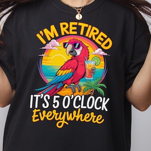May include: Black t-shirt with a colorful graphic of a parrot wearing sunglasses, holding a cocktail, and the text "I'M RETIRED IT'S 5 O'CLOCK Everywhere". The design features a sunset and palm tree.