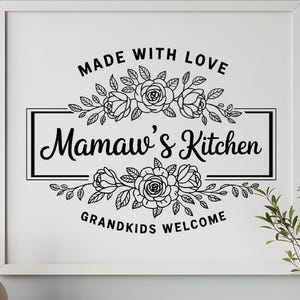 May include: A framed print with the text "Made With Love, Mamaw's Kitchen, Grandkids Welcome" in a black script font. The text is surrounded by floral designs. The print is in a white frame.