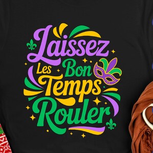 May include: Black t-shirt with the phrase "Laissez Les Bon Temps Rouler" in purple, green, and yellow. A Mardi Gras mask graphic is included. The shirt is a classic crew neck style.