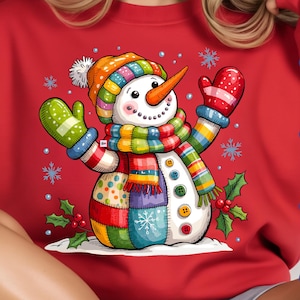 Puede incluir: Una sudadera roja con un diseño de muñeco de nieve colorido. El muñeco de nieve tiene una nariz de zanahoria, un cuerpo de retazos y lleva un sombrero, una bufanda y mitones. La imagen también incluye copos de nieve y el texto "PNG DAWNLAND", "SVG DAWNLAND", "EPS DAWNLAND" y "PDF DAWNLAND".