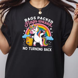 Könnte beinhalten: Schwarzes T-Shirt mit einem bunten Einhorn-Motiv, das einen Koffer und einen Cocktail hält, vor einem Regenbogen. Der Text lautet: "BAGS PACKED, Flaps waxed, NO TURNING BACK."