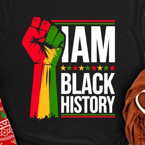 May include: Black t-shirt with a raised fist in red, green, and yellow, and the words "I AM BLACK HISTORY" in white. The design includes green and gold stars and red and green stripes.