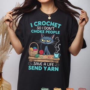 Peut inclure: T-shirt noir avec le texte "I CROCHET SO I DON'T CHOKE PEOPLE SAVE A LIFE SEND YARN". Le t-shirt présente un chat de dessin animé, de la laine et une tasse à thé. Le t-shirt est de style décontracté et confortable.
