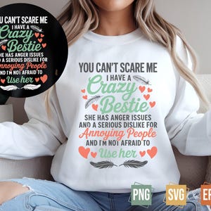 May include: White sweatshirt with a green and pink graphic design that says "You can't scare me I have a crazy bestie she has anger issues and a serious dislike for annoying people and I'm not afraid to use her".