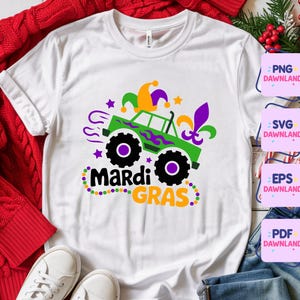 May include: White t-shirt featuring a green monster truck design with black wheels, purple and green accents, and the words "Mardi Gras" in black and orange. The design includes a jester hat and fleur-de-lis.