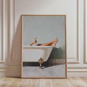 May include: Framed art print depicting a person relaxing in a white claw-foot bathtub, holding a glass of white wine. The artwork features a light blue background and a gold-colored frame. The image evokes a sense of leisure and tranquility.