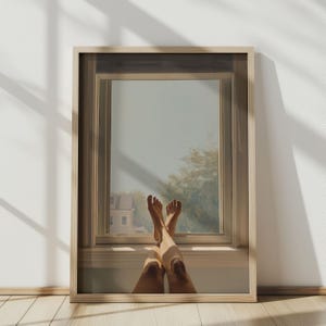 Puede incluir: Una impresión enmarcada que muestra las piernas y los pies de una persona descansando en un alféizar, con una vista de una casa y árboles afuera. El marco es de color claro y la habitación tiene un suelo de madera. La ventana es el foco de la imagen.