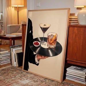 Pode incluir: Uma impress&atilde;o de arte emoldurada apresentando um disco de vinil preto usado como bandeja. O disco sustenta uma ta&ccedil;a de martini com gr&atilde;os de caf&eacute;, um copo com casca de laranja e uma pequena tigela branca cheia de cerejas vermelhas brilhantes.