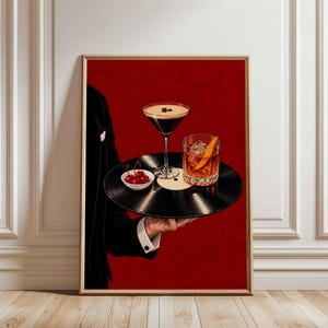 May include: A framed wall art print featuring a person in a black suit jacket holding a black vinyl record as a serving tray. On the record sits a martini glass with coffee beans, a rocks glass with an orange peel, and a small bowl of red cherries.