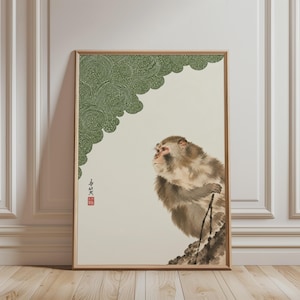 Op de afbeelding: Een ingelijste kunstdruk met een bruine en beige aap die op een rotsachtig oppervlak zit. De linkerbovenhoek toont een groen patroon van concentrische cirkels. Een rood zegel en zwarte kalligrafie zijn zichtbaar aan de linkerkant van de print.