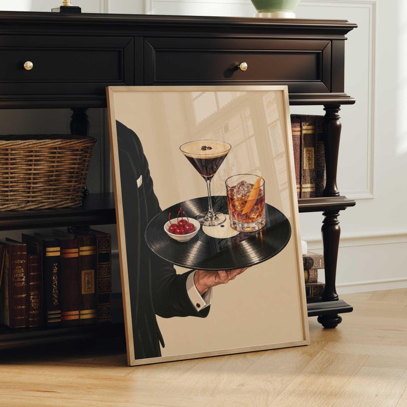 Pode incluir: Uma impress&atilde;o art&iacute;stica emoldurada mostrando uma pessoa com um palet&oacute; preto segurando um disco de vinil preto como bandeja. O disco cont&eacute;m uma ta&ccedil;a de martini com gr&atilde;os de caf&eacute;, um copo de u&iacute;sque com gelo e casca de laranja e uma tigela.