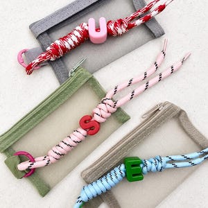 Può includere: Quattro piccole pochette rettangolari con frontali in rete e accenti colorati. Ogni pochette ha un cordino di colore diverso con un ciondolo a forma di lettera: cordino rosso e bianco con una "U" rosa, cordino rosa con una "S" rossa e cordino blu con una "E" verde.