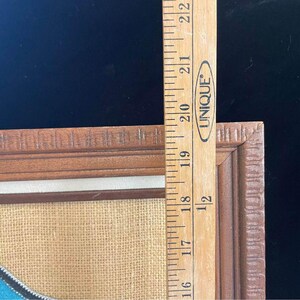 May include: A framed piece of art with a blue, white, and brown design on a burlap background. The frame is made of wood and has a decorative edge.