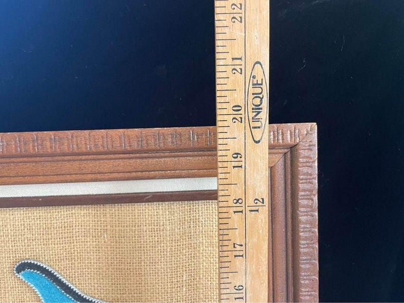 May include: A framed piece of art with a blue, white, and brown design on a burlap background. The frame is made of wood and has a decorative edge.