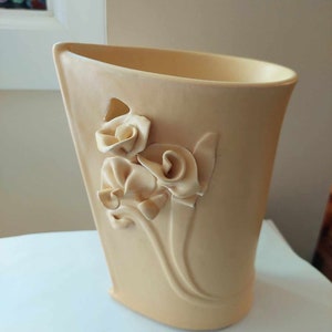 May include: A pale yellow ceramic vase with a decorative floral design. The vase has a wide mouth and a rounded bottom.