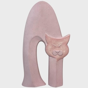 May include: A pale pink ceramic sculpture shaped like an arched cat with a speckled texture. The piece features a tall, curved back forming an arch and a distinct cat head with pointed ears and a simple facial expression, all in a uniform pink tone.