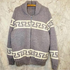 May include: A grey knitted zip-up sweater with a white geometric pattern. The sweater has a collar and long sleeves.