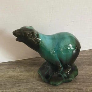 Puede incluir: Una figura de cerámica de un oso en posición erguida, con un esmalte brillante que presenta tonos mezclados de verde bosque profundo y azul turquesa vibrante. El oso está esculpido con la cabeza ligeramente girada sobre una base verde.