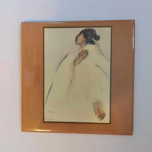 May include: A framed artwork featuring a sketch of a person in a flowing white garment. The person is depicted in profile, with dark hair and a turquoise earring. The artwork is set against a light background, framed in a warm brown.