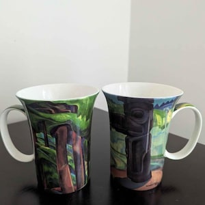 Peut inclure: Deux mugs en céramique avec des anses et intérieurs blancs. L'un présente une scène de forêt verte et marron, l'autre un totem noir sur fond bleu et vert. Les deux mugs ont une finition brillante.