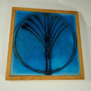 May include: A framed blue ceramic tile with a black abstract design of a tree in a circle.