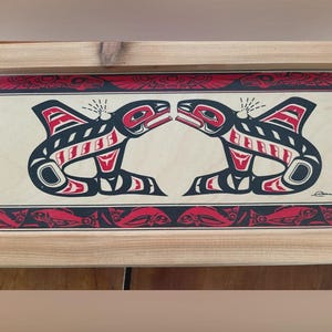 May include: A rectangular wooden wall art piece featuring a light-coloured wood frame. The central panel displays a black and red graphic design of two mirrored orca whales facing each other, with a border of stylised fish patterns above and below.