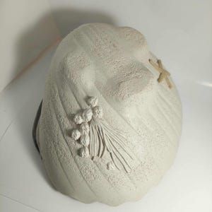 May include: A textured off-white ceramic bowl with a matte finish. The exterior features a raised relief design of a small starfish and a cluster of round berries with thin stems. The bowl has a curved, organic shape with a scalloped edge.