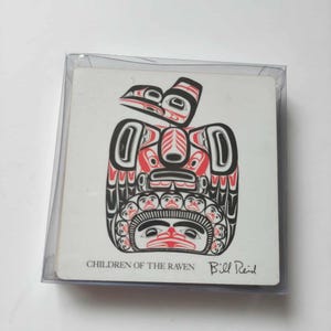 Op de afbeelding: Een vierkante onderzetter in een doorzichtig plastic hoesje met een zwart en rood grafisch ontwerp genaamd Children of the Raven door Bill Reid. Het kunstwerk toont gestileerde figuren en gezichten in een symmetrisch patroon.