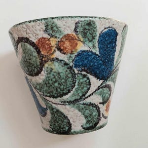 May include: A small, white ceramic bowl with a green, blue and orange floral pattern. The bowl has a textured surface and a slightly flared rim.
