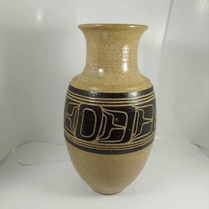May include: A tan ceramic vase with a wide base and a narrow neck. The vase features a black geometric design around the middle. The vase is approximately 25 cm tall.
