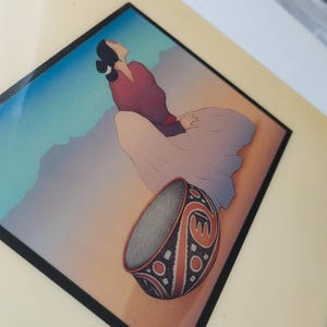 May include: An artistic print depicting a woman in a flowing dress gazing upwards. The artwork includes a detailed, patterned bowl in the foreground. The colour palette includes shades of red, blue, and beige, creating a serene and contemplative scene.